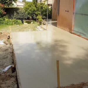 Dalle béton fraîchement coulée pour une future terrasse, avec les coffrages en bois, dans un jardin ensoleillé.