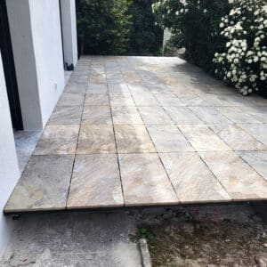 Terrasse moderne avec carrelage de grandes dalles aspect pierre naturelle, près d'un mur blanc et jardin verdoyant.