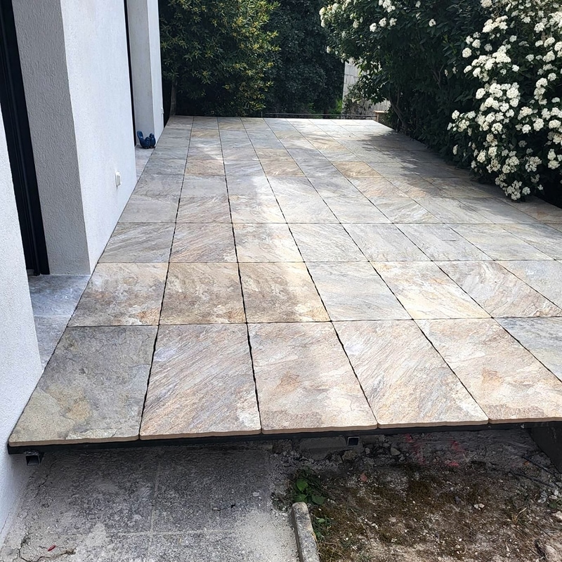 Terrasse moderne avec carrelage de grandes dalles aspect pierre naturelle, près d'un mur blanc et jardin verdoyant.