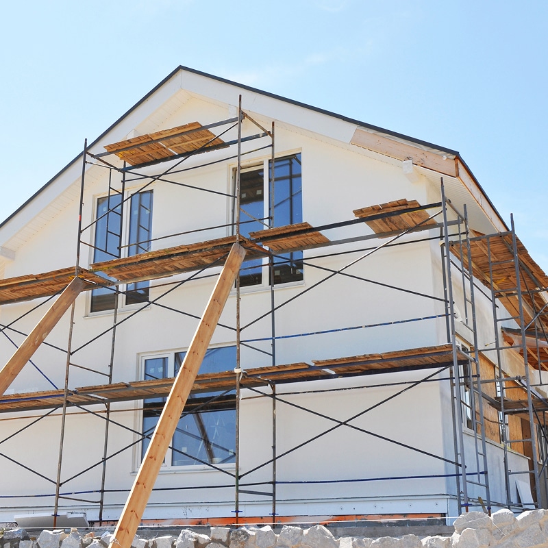 Maison blanche neuve ou en rénovation avec échafaudage métallique et planches de bois. Travaux de façade sous ciel bleu dégagé.
